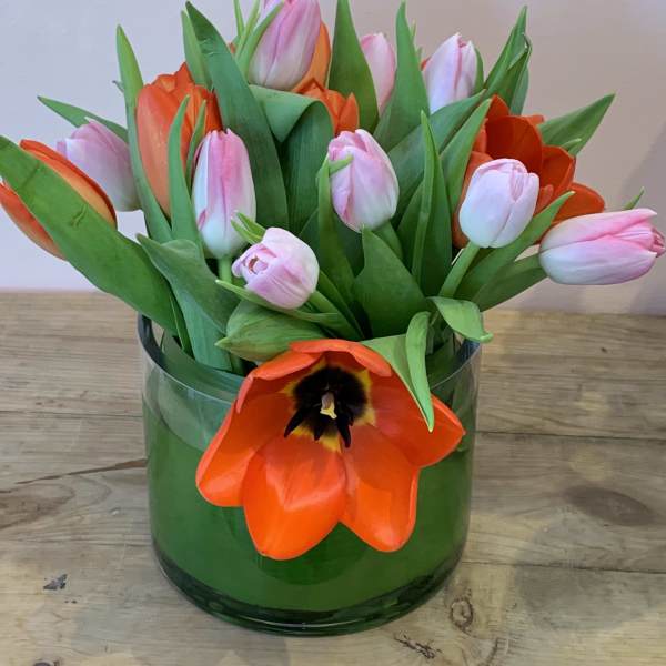 Pink and orange tulips arranged in a green glass vase