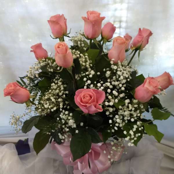 Pink roses arranged in a bouquet with baby's breath and a pink ribbon