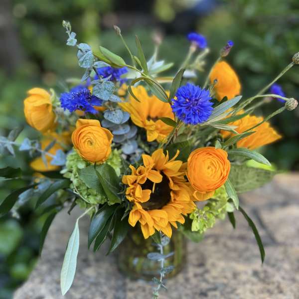 Bouquet of yellow sunflowers and blue flowers in a glass vase