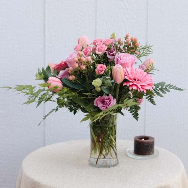 Pink mixed bouquet in a clear glass vase beside a small candle