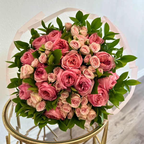 Round bouquet of pink roses with green foliage wrapped in pale paper