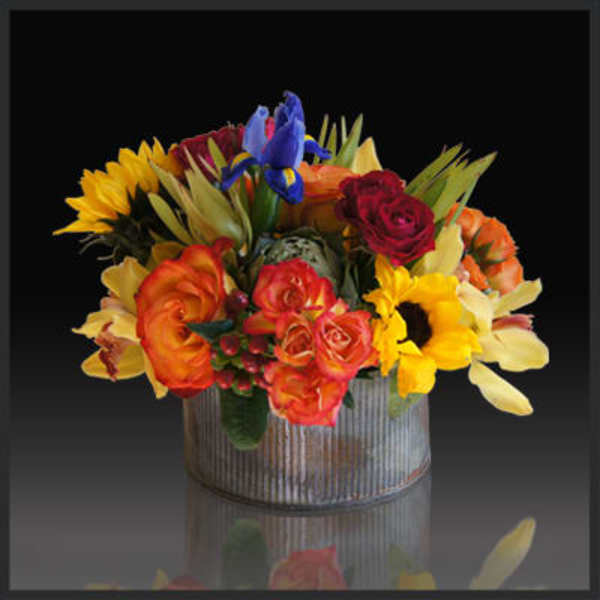 Colorful bouquet in a ribbed metal container with sunflowers and roses