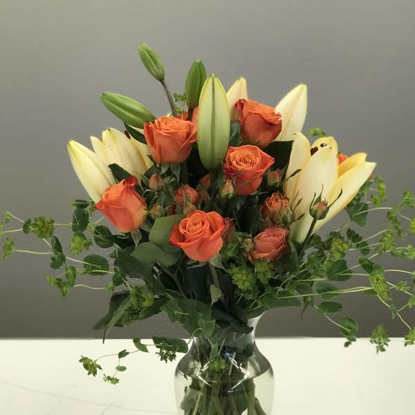 Orange roses and cream lilies in a glass vase