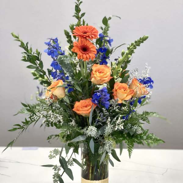Orange roses and blue flowers in a tall glass vase