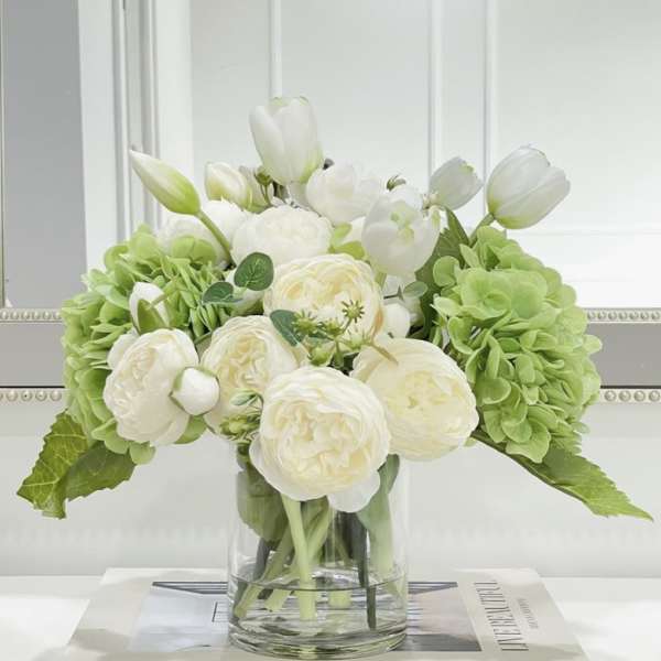 White tulips and cream roses in a clear glass vase with green hydrangeas