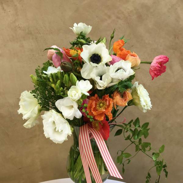 Mixed bouquet of white, orange, and pink flowers in a glass vase with a striped ribbon