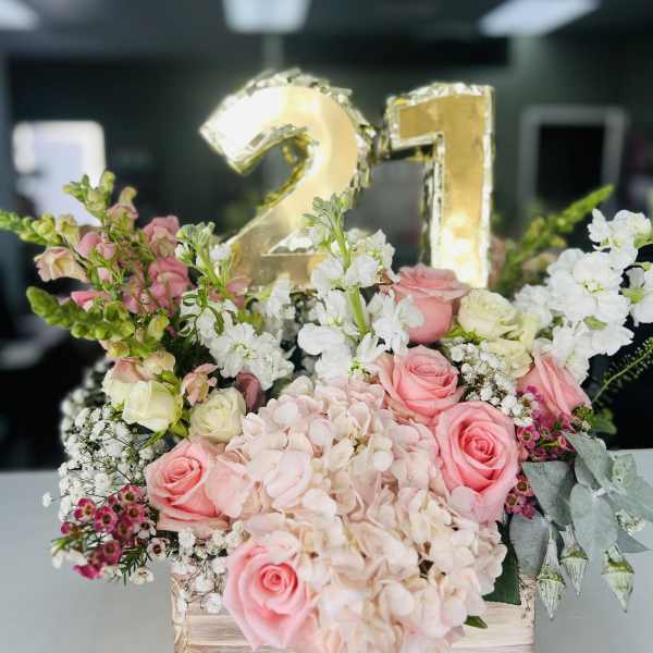 Pink and white floral arrangement with a gold "21" balloon