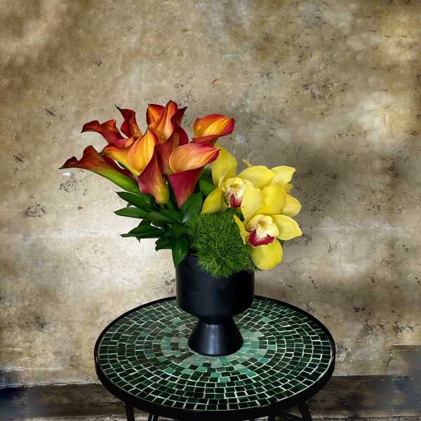 Arrangement of red-orange calla lilies and yellow orchids in a black vase