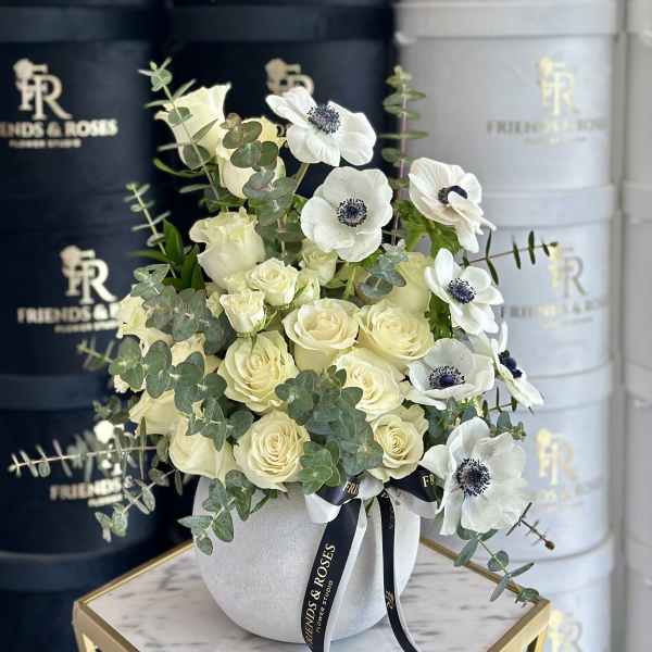 Cream roses and white anemones in a white vase with eucalyptus