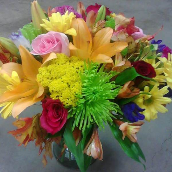 Colorful mixed bouquet with roses, lilies, and daisies in a glass vase