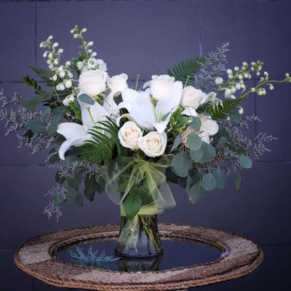 White lilies and roses arranged in a glass vase with greenery