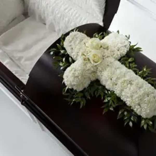 White floral cross arrangement on a dark casket