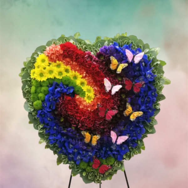 Heart-shaped floral wreath with rainbow flowers and butterfly accents on a stand