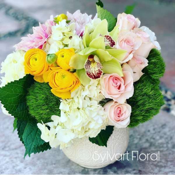 Mixed bouquet of pink roses, yellow ranunculus, and white orchids in a white vase