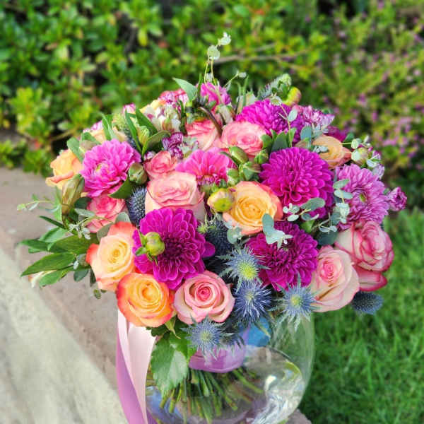 Bouquet of pink and peach roses with purple blooms in a glass vase