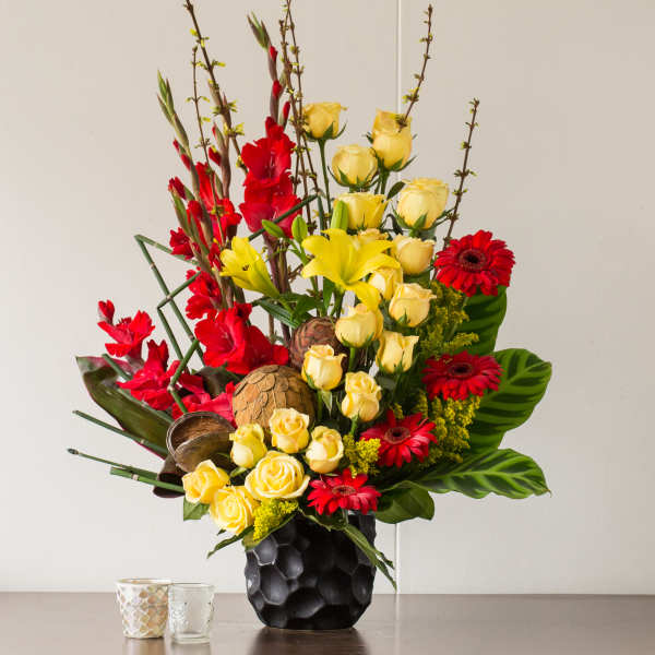 Tall bouquet of yellow roses, red flowers, and lilies in a black vase