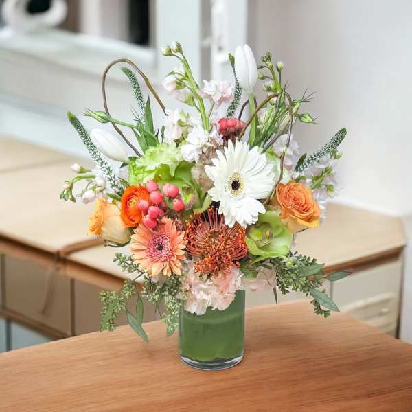 Mixed bouquet in a green glass vase with white, peach, and orange flowers