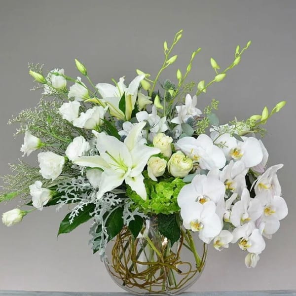 White floral arrangement in a clear glass vase with orchids and lilies