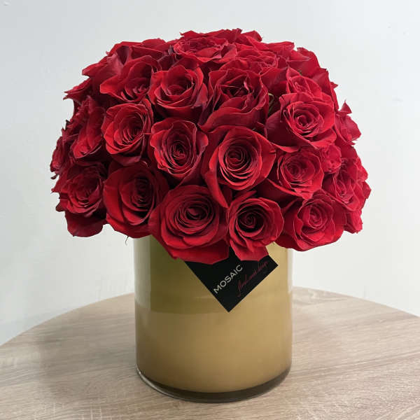 Dense arrangement of red roses in a cylindrical tan glass vase