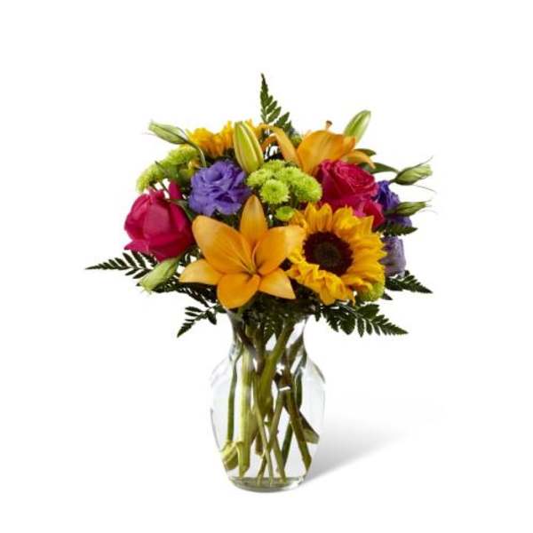 Bright mixed bouquet with lilies, sunflower, roses, and lisianthus in a clear glass vase