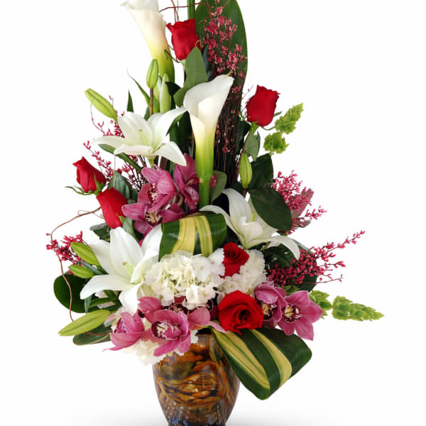 Tall bouquet of white calla lilies, red roses, and pink orchids in a glass vase