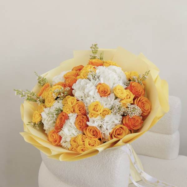 Bouquet of orange and yellow roses with white flowers wrapped in yellow paper