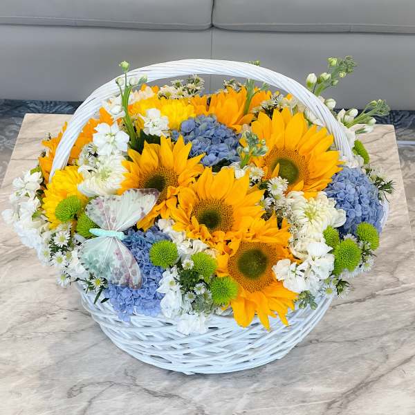 Basket of sunflowers, blue hydrangeas, and white flowers with a butterfly decoration