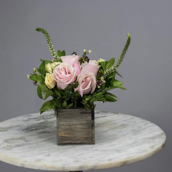 Pink roses in a wooden box with greenery and tall accent stems