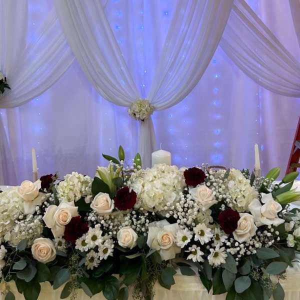 White floral wedding backdrop with draped fabric and a matching flower-covered table
