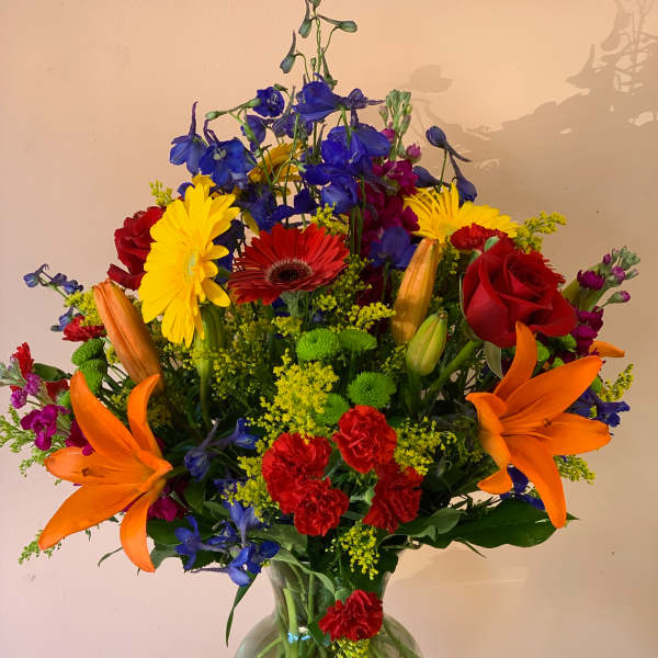 Colorful mixed bouquet in a clear glass vase with lilies, roses, and daisies