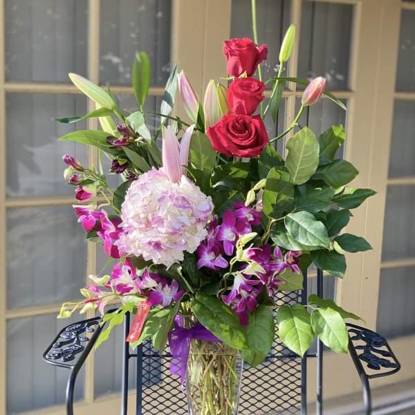 Bouquet of red roses, pink lilies, and orchids in a clear glass vase