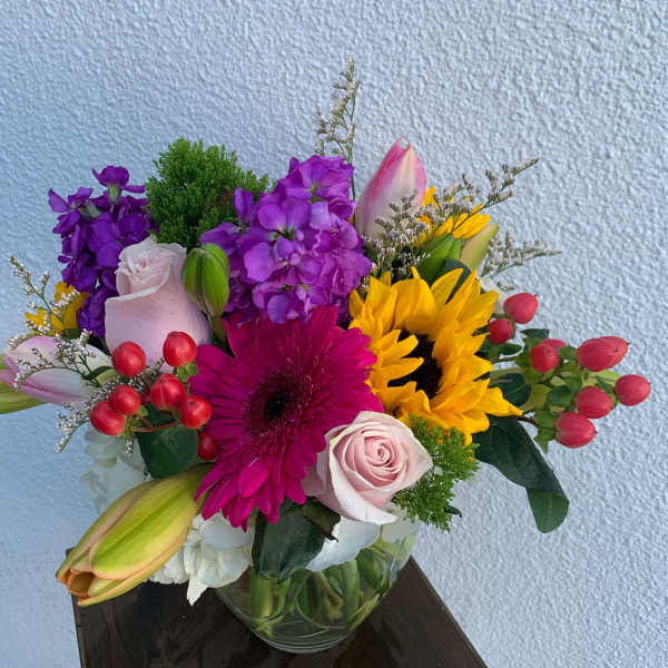 Colorful mixed bouquet with sunflowers, roses, lilies, and a gerbera daisy in a glass vase