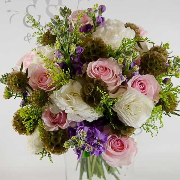 Pink and white roses with purple flowers in a clear glass vase
