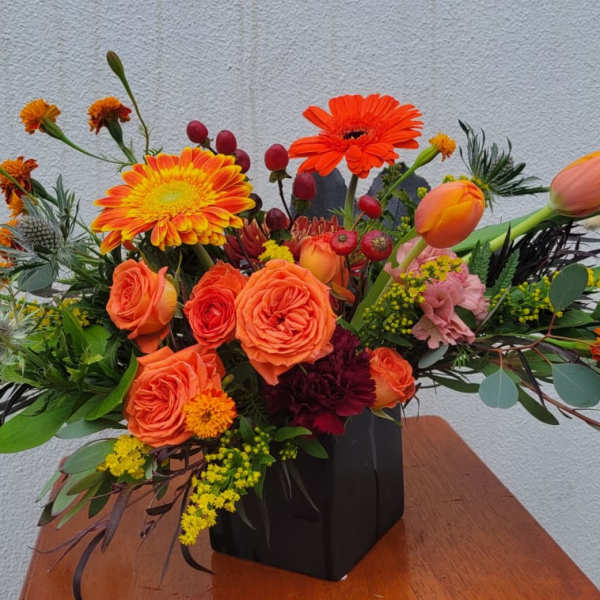 Orange and yellow mixed flower arrangement in a black vase
