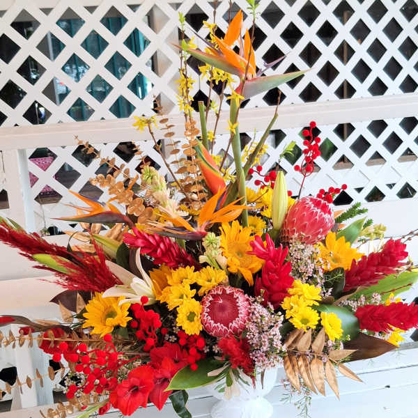 Large tropical bouquet with red, yellow, and orange flowers in a white vase