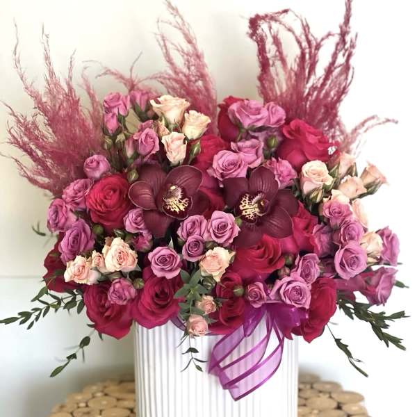 Pink and red rose arrangement in a white vase with a purple ribbon