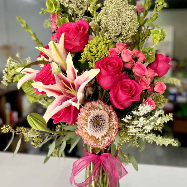 Pink roses and lilies in a glass vase with a pink ribbon