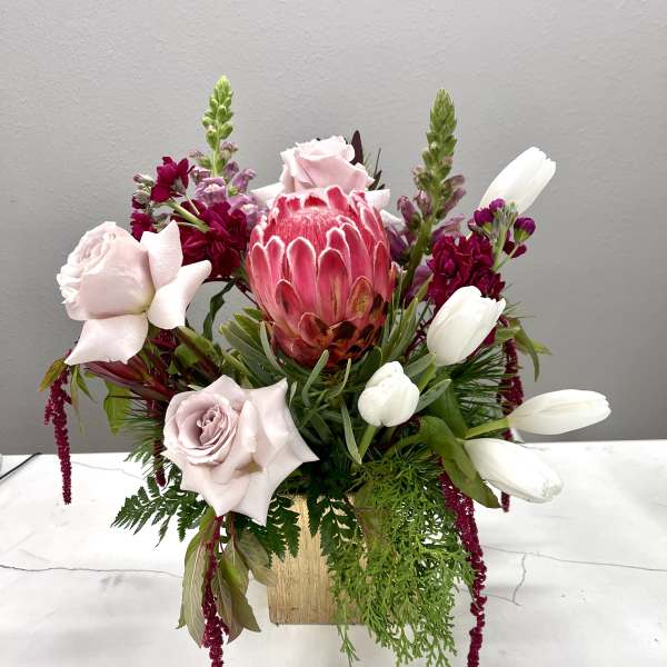 Mixed bouquet with pink protea, pale roses, and white tulips in a gold vase