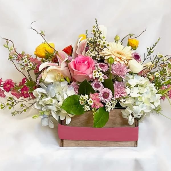 Mixed flower arrangement in a wooden box with pink ribbon