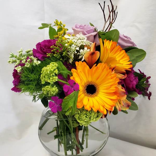 Colorful bouquet with orange gerbera daisies and lavender roses in a glass vase