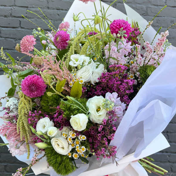 Hand-tied bouquet of pink, white, and purple flowers wrapped in white paper