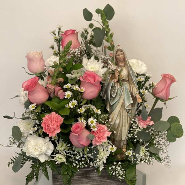 Pink roses and white flowers arranged around a religious statue in a box.
