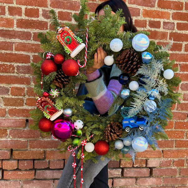 Person holding a decorated Christmas wreath with ornaments and pinecones