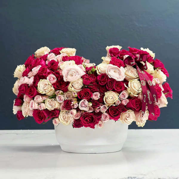 Large arrangement of pink, cream, and red roses in a white container