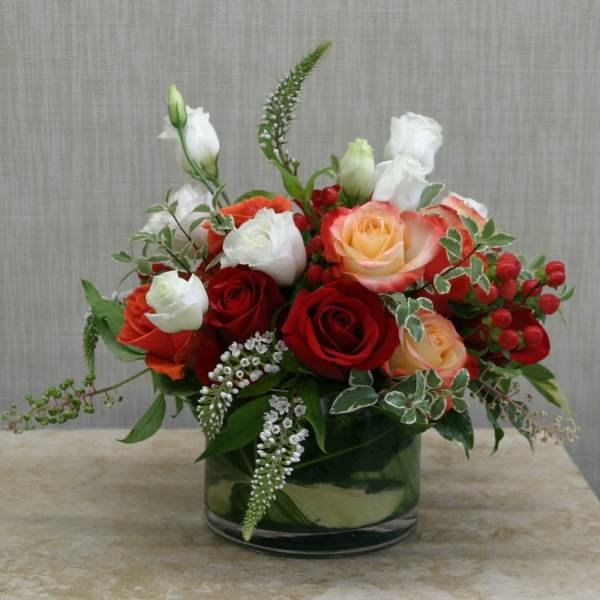 Mixed rose bouquet in a glass vase with white blooms and red berries