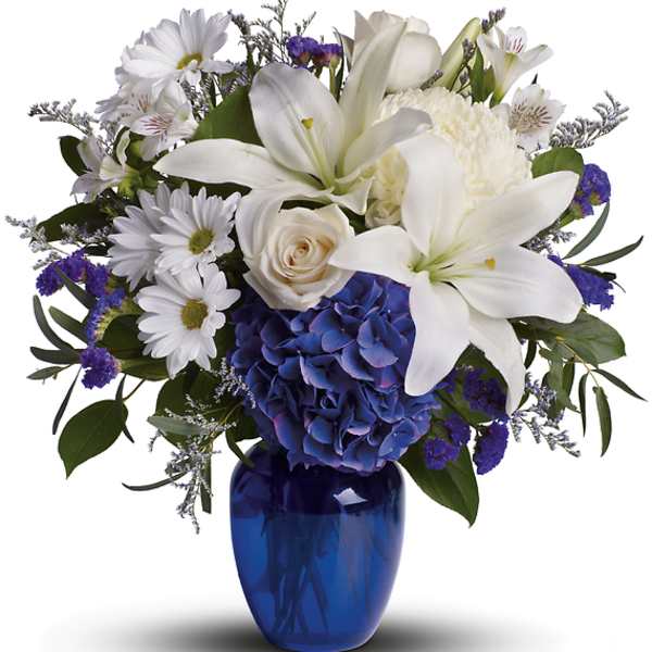 White lilies, roses, daisies, and blue hydrangea in a cobalt vase