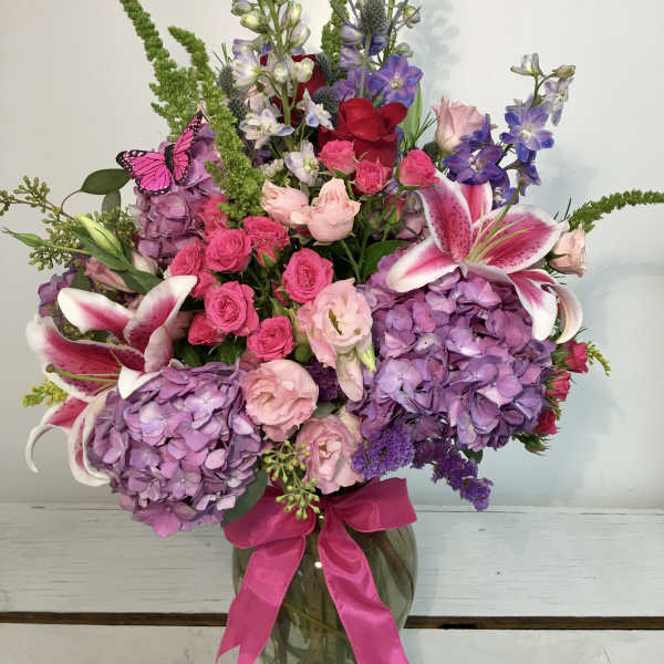 Large bouquet of pink, purple, and white flowers in a glass vase with a ribbon