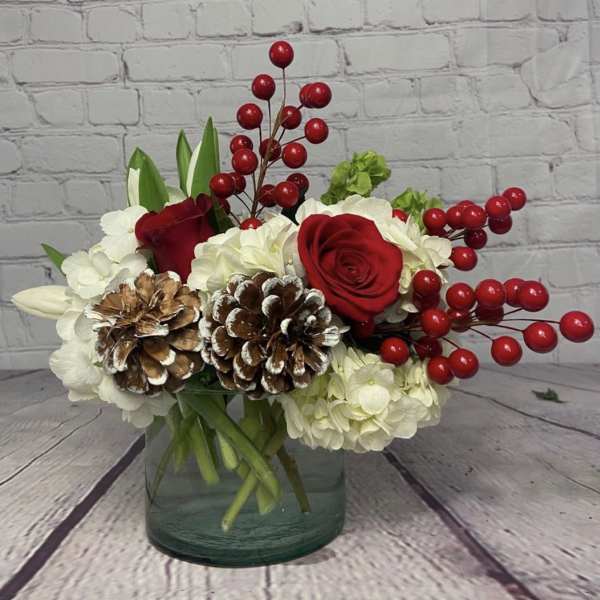 Red roses and white hydrangeas in a glass vase with pinecones and red berries