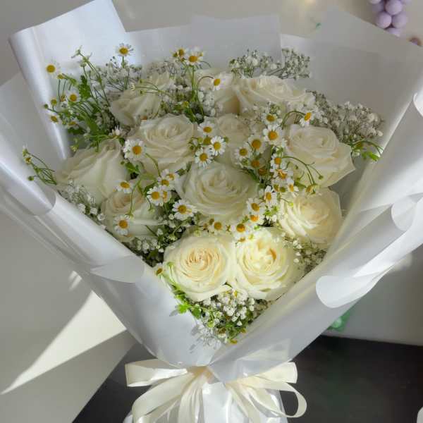 Bouquet of white roses and small daisy flowers wrapped in white paper