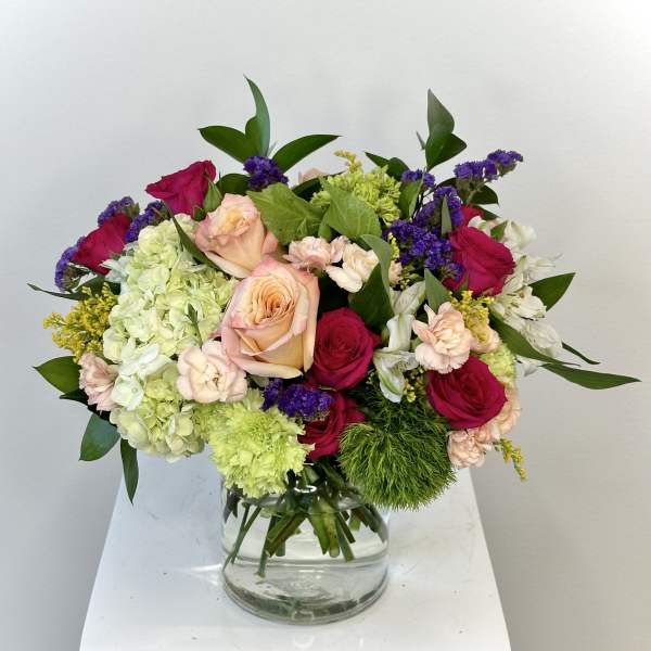 Mixed bouquet of roses, hydrangeas, and carnations in a glass vase